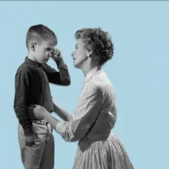 Imagem em preto e branco com fundo azul claro. À esquerda, um menino pequeno, de pé, enxuga uma lágrima do rosto com a mão. À direita, uma mulher ajoelhada segura delicadamente o menino pela cintura e o observa com expressão atenta e acolhedora