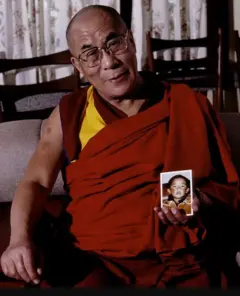 Dalai Lama usando roupa vermelha e segurando a foto do menino que foi identificado como Panchen Lama e desapareceu