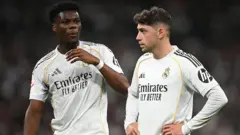 Real Madrid's Aurelien Tchouameni and Federico Valverde stand next to each other in a match, wearing the club's white kit