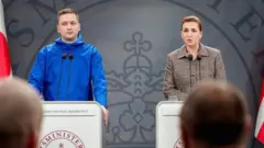 Mette Frederiksen, con una chaqueta marrón, y el primer ministro de Groenlandia, Jens-Frederik Nielsen, con un impermeable azul, hablan con los periodistas, con las banderas de Dinamarca y Groenlandia a los lados de los dos podios.