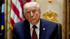 ダークスーツ姿のトランプ氏が少し首を傾けて前方を見ている。背後には米国旗が見える