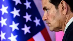 O secretário de Estado dos EUA, Marco Rubio, visto de perfil, com uma bandeira americana ao fundo