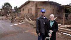Mãe e filho em frente a casa destruída