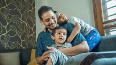 Young father laughing and playing with cute sons while sitting on sofa in living room during weekend