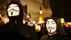 Masked protesters (protestors, demonstrators), wearing a Guy Fawkes masks demonstrate in front of the Houses of Parliament during the Million Mask March in Parliament Square on November 5, 2015 in London