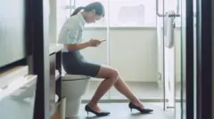 Mulher sentada no vaso sanitário usando o telefone celular