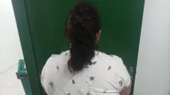 Mujer arrestada, de espaldas frente a una puerta verde