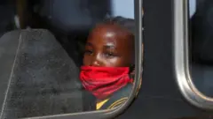 A girl wearing a mask looks on through a bus window in Eikenhof, south of Johannesburg, South Africa. Photo: August 2020