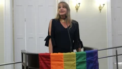 Marina Reidel fala em tribuna, na qual está pendurada bandeira do arco-íris