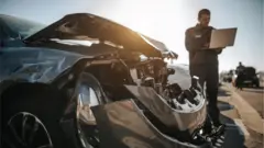 Un mecánico con un ordenador evalúa un vehículo accidentado