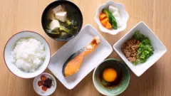 Mesa de refeição com potes contendo arroz, peixe, ovo e outros alimentos