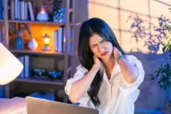 এক নারী চোখ কুচকে দুই হাতে ঘাড় ধরে আছে।