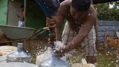 Joven llena garrafas de agua de manguera de camión cisterna