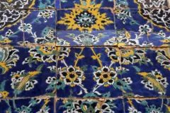 Azulejos islâmicos, com padrões detalhados, rachados devido à tensão. Eles apresentam motivos florais em azul, amarelo, preto e branco.