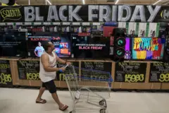Homem anda com carrinho de compras em uma loja cheia de placas de promoção da Black Friday