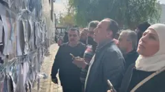 صورة تظهر أفراد عائلات وأصدقاء السجناء المفقودين في سوريا يدققون النظر في جدار مليء بصور مطبوعة لرجال متوفين معلقة على جدار خارج مستشفى المجتهد في دمشق.