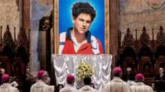 Un tapiz de Carlo Acutis, un adolescente, y personas con atuendos religiosos mirando.