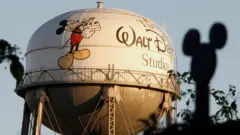 Torre de água da The Walt Disney Co., com o personagem Mickey Mouse, é vista atrás de uma silhueta de cabeça e orelhas de rato na cerca que protege a sede da empresa em Burbank