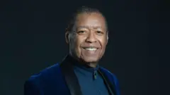 Ron Kenoly wear one dark blue blazer with one blue sweat shirt