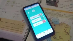 یک کتاب مدرسه به زبان فارسی باز است و یک موبایل روی آن، در صفحه موبایل مراحل ورود به فضای مجازی آموزش نشان داده شده است