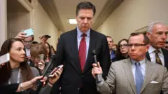 James Comey en 2019 camina rodeado de reporteros, algunos poniéndole micrófonos para conseguir su testimonio