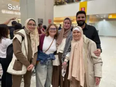 Cinco pessoas reunidas e sorrindo em saguão de aeroporto