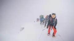 Bir dağcı oldukça dik bir yerde tüm vücudu korumalı bir şekilde tırmanıyor. 