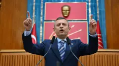 Özgür Özel, Meclis'teki grup toplantısında kürsüde konuşuyor. Arkasında Atatürk büstü ve CHP'nin altı oklu amblemi var