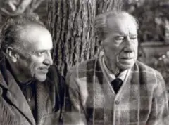 Dos hombres mayores, vestidos casualmente, sentados frente a un árbol