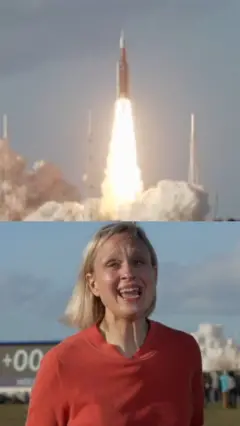 රොකට්ටුවක් දුම් නගමින් ඉහල නගින අතර ඊට පහලින් තැඹිලි පැහැති ඇඳුමකින් සැරසුණු කාන්තාවක් සිටී.