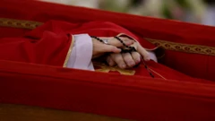 Las manos entrelazadas del Papa sostienen un rosario negro. 