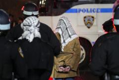 Mulher algemada com lenço árabe, ao lado de policiais