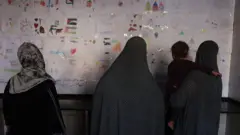 نساء يتأملن مجموعة من الرسومات التي رسمها أطفال في إحدى مدارس النزوح