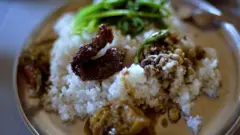 Prato de comida indiano com arroz, um pedaço de carne e um vegetal