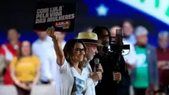 Janja e Lula no palco vestidos de branco. Janja segura um cartaz escrito "Com Lula pela vida das mulheres".
