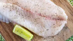 Um filé de peixe branco com pimenta por cima e um limão ao lado