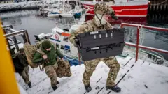 Danimarkalı askerler ellerinde askeri çanta ve kutularla deniz kenarındaki bir merdivenden çıkıyor. 