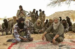 Des rebelles touaregs assis sur un tapis sous un arbre, entourés de combattants.