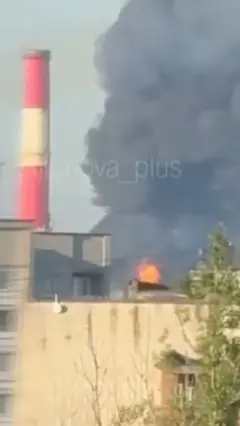 Скриншот с видео очевидца удара по НПЗ: крыши домов, за ними - столб дыма и пламя огня.
