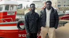 Ibrahima Diack y Magatte N'Diaye en el puerto deportivo de La Coruña con un barco rojo detrás. 