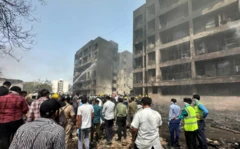 Grupo de pessoas no local de acidente aéreo, com água sendo lançada em prédio danificado por fogo