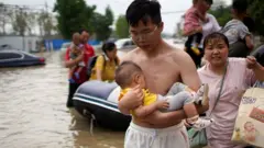 A man holding a baby wades through a flooded road following heavy rainfall in Zhengzhou, Henan province, China July 22, 2021