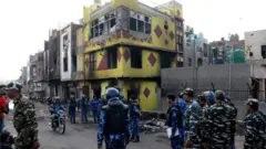 एक जले हुए मकान के बाहर खड़े सुरक्षाकर्मी