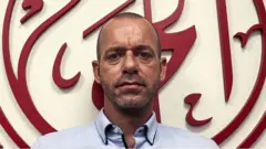 صلاح حموري، المحامي الفلسطيني الذي يحمل الجنسيتين الفلسطينية والفرنسية، يقف أمام شعار لمؤسسة الحق لحقوق الإنسان في رام الله بالضفة الغربية في صورة تعود إلى نوفمبر/ تشرين الثاني 2021