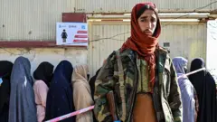 A Taliban fighter stands guard as women wait in line during a World Food Programme food distribution in Kabul