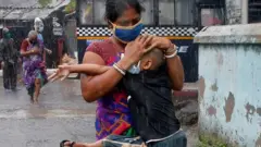 Una mujer corre debajo de la lluvia con un niño en brazos en Calcuta.