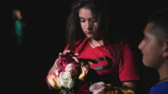 A young girl holds flowers outside the Willie de Leon Civic Center where people gather to mourn in Uvalde, Texas, 24 May 2022
