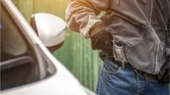 Foto de banco de imagens mostra homem tirando arma de bolso ao lado de um carro