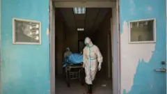 Médicos carregam paciente morto pelo coronavírus na China