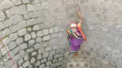 A still from the video showing woman scaling the wall of a well without any support
